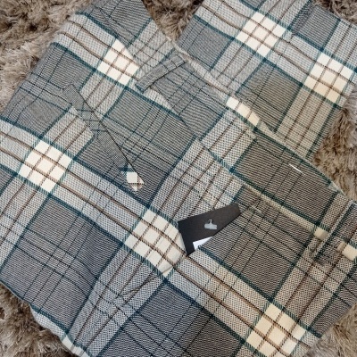 Calças xadrez cinza branco verde com etiqueta preta sobre tapete castanho