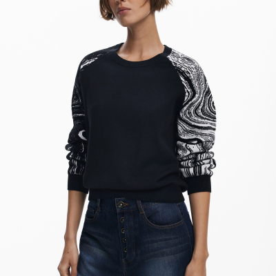 Mulher com camisola preta de manga comprida com padrão preto e branco e jeans azul escuro