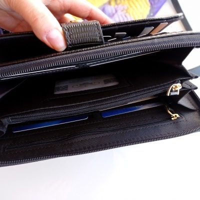 Carteira preta de material sintético aberta com divisórias internas e fecho de correr dourado