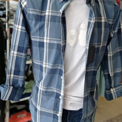 Manequim com camisa xadrez azul aberta sobre t-shirt branca e jeans azuis em loja