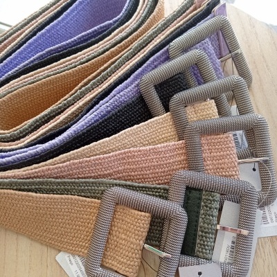 Vários cintos trançados coloridos com fivelas quadradas prateadas numa mesa de madeira