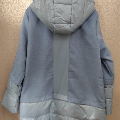 Casaco azul claro com capuz pendurado em cabide num fundo bege decorativo