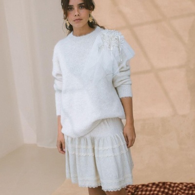 Mulher com camisola branca de malha com aplicação de tule e pérolas, saia branca com renda e botins castanhos
