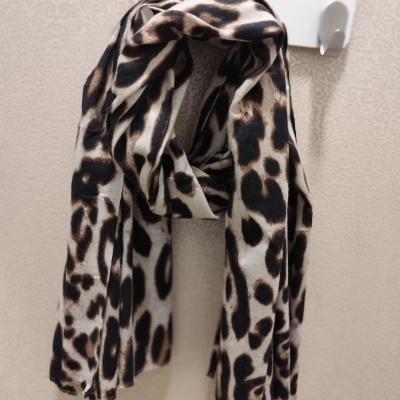 Cachecol animal print castanho e preto pendurado num suporte branco com a palavra Modas