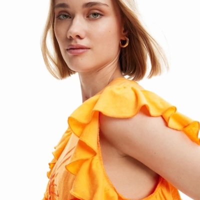 Mulher de cabelo loiro curto com vestido laranja com folhos e argola dourada