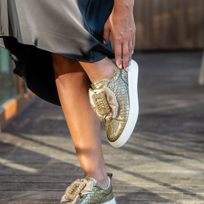 Ténis dourados com padrão tipo pele de crocodilo e detalhes em tecido bege com pérolas