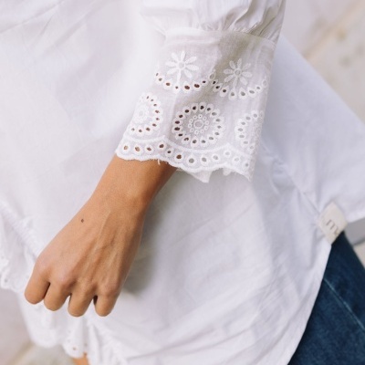 Camisa branca com punhos bordados em padrão floral e calças azuis