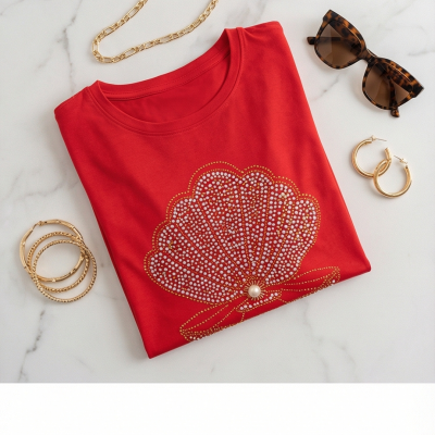 T-shirt vermelha com padrão de concha brilhante e acessórios dourados sobre mármore