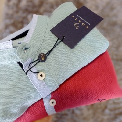 Duas polos COATI em algodão, verde claro com gola branca e rosa, com etiquetas e botões.