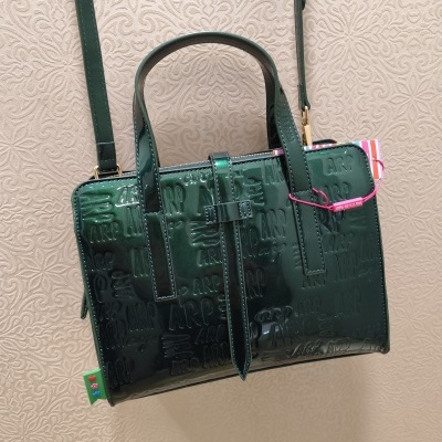 Mala de mão verde escura com padrão ARP em relevo e fundo creme texturizado