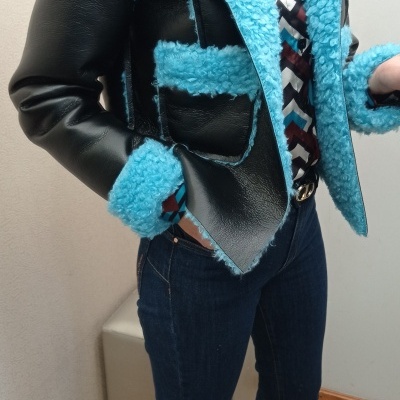 Casaco de pele sintética preta com detalhes felpudos azuis e camisa estampada, usado com calças de ganga.