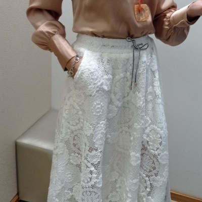 Camisa cetim bronze com gola ampla e saia renda branca midi com cinto, colar pendente, tapete bege e banco cinzento