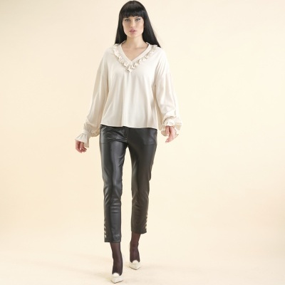 Mulher vestindo blusa branca com babados e calças pretas de couro