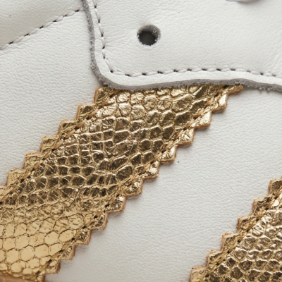 Ténis branco com padrão dourado texturizado e sola de borracha castanha