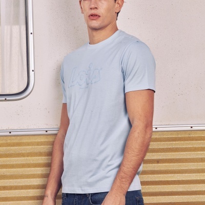 Homem com t-shirt azul clara e calças de ganga em fundo de parede cream e amarelo com janela