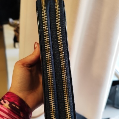 Carteira preta com dois fechos dourados vista de lado nas mãos