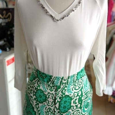 Conjunto com blusa branca de manga comprida decorada com cristais e parte inferior verde estampada.