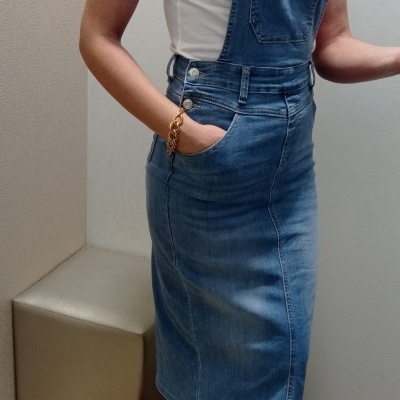 Vestido salopete de ganga azul com t-shirt branca e sapatilhas coloridas junto a um pufe bege