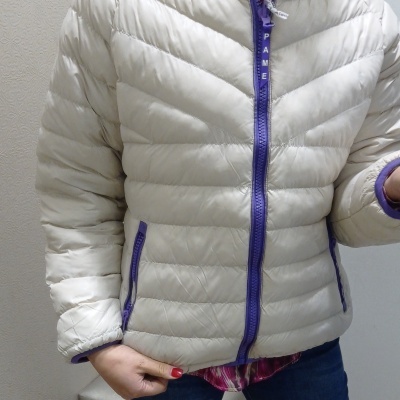 Casaco acolchoado bege com fecho roxo e bolsos laterais.
