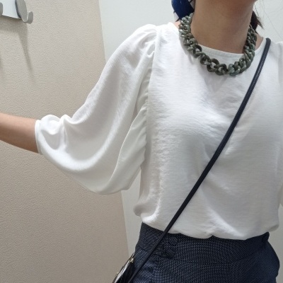 Blusa branca com mangas bufantes, calça azul escura e colar verde em corrente