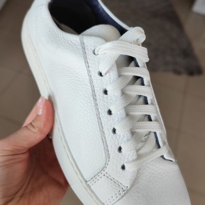 Tênis branco de couro sintético com atacadores brancos em ambiente interior