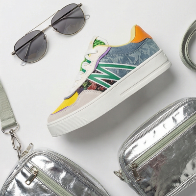Tênis colorido com óculos de sol e bolsas prateadas sobre fundo branco