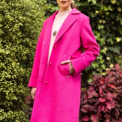 Casaco feminino longo rosa vibrante com camisola rosa clara e colar, em exterior com folhagem