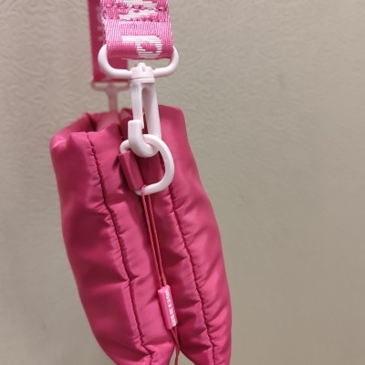 Bolsa pequena cor-de-rosa acolchoada com alça rosa e texto branco num fundo bege