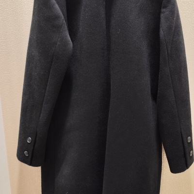 Casaco preto com gola de pelo branco pendurado numa parede clara