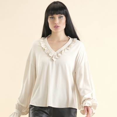 Blusa creme feminina de tecido leve com folhos na gola e punhos franzidos, calças pretas sintéticas.