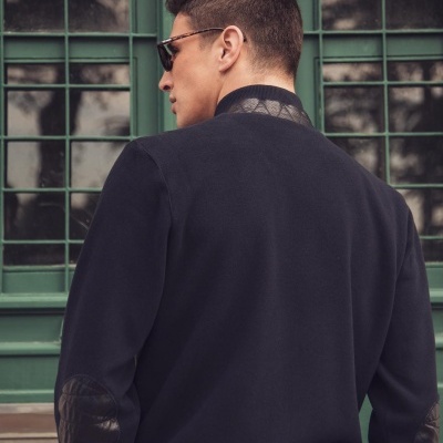 Homem de costas com casaco preto com detalhes em couro e óculos de sol