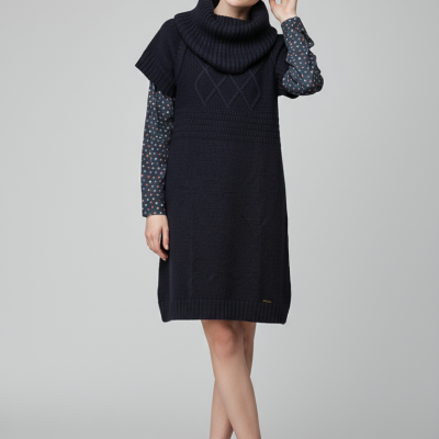 Mulher com vestido de malha azul escuro, camisa com padrão de círculos e botas pretas