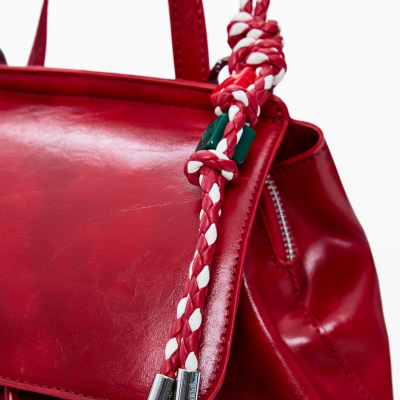 Mala vermelha de pele com alça superior e corda trançada vermelha e branca com pontas metálicas.