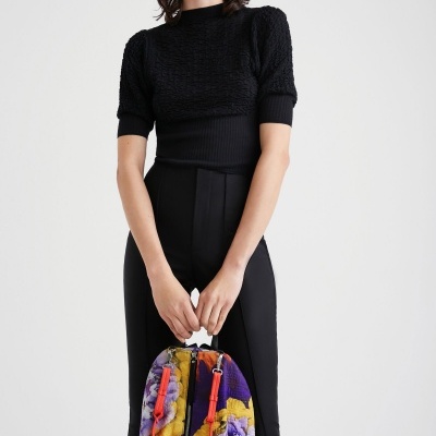 Mulher de blusa preta e calças pretas segurando mochila colorida