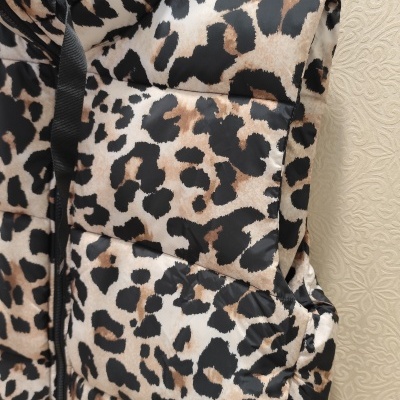 Colete acolchoado com padrão animal print castanho, preto e bege pendurado em cabide.