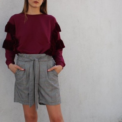 Mulher a usar calças curtas xadrez cinza e camisola bordeaux com volantes