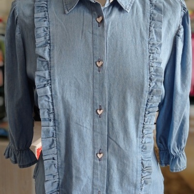 Camisa de ganga azul clara com volantes e botões em forma de coração num manequim