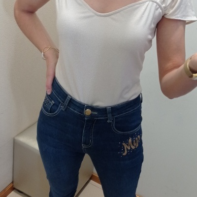 Pessoa com t-shirt branca brilhante e jeans azuis justos com bordado dourado