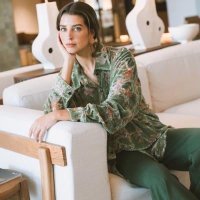 Mulher sentada num sofá branco com camisa verde floral e calças verdes