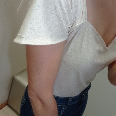 Pessoa com t-shirt branca brilhante e jeans escuros num ambiente interior.