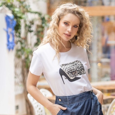 Mulher com t-shirt branca estampada com mala e sapato e saia azul em ambiente exterior