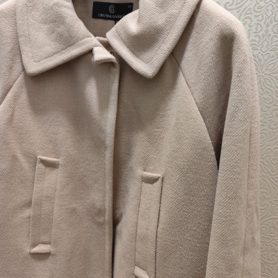 Casaco bege claro de tecido felpudo com gola e bolsos, pendurado num cabide.