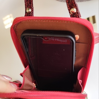 Mala pequena vermelha aberta com interior castanho e telemóvel preto dentro