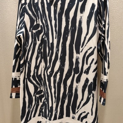 Vestido riscas preto e branco com detalhes castanhos numa parede bege texturizada.