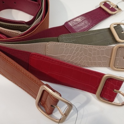 Cinco cintos de couro com textura croco em várias cores e fivelas douradas sobre fundo branco