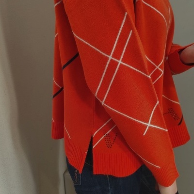 Camisola laranja com padrão de linhas brancas e pretas em ambiente interior.