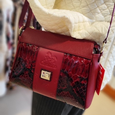 Mala vermelha com padrão pele de cobra, marca Cavallinho, em manequim com casaco creme acolchoado.