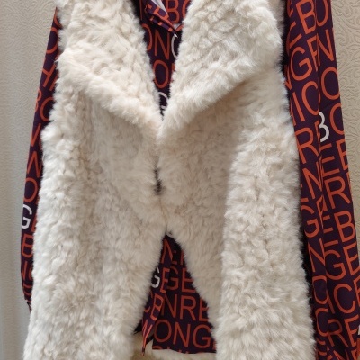 Colete branco de pelo sintético sobre camisola colorida pendurados em cabide preto com inscrição