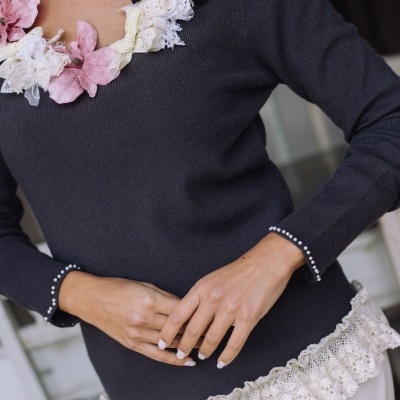 Blusão feminino preto com flores de tecido no decote e renda branca na barra em ambiente interior