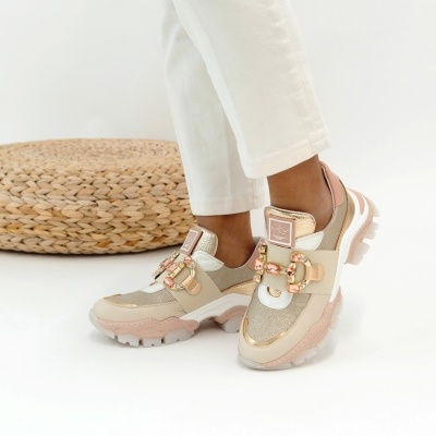 Ténis bege e dourados decorados com pedras, usados por pessoa com calças brancas, fundo branco e objecto de palha.